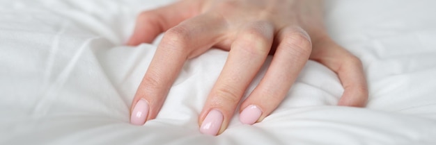 La mano di una donna sta stringendo una coperta sul letto