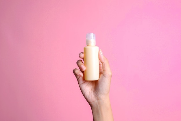 La mano di una donna tiene elegantemente una bottiglia di crema su uno sfondo rosa