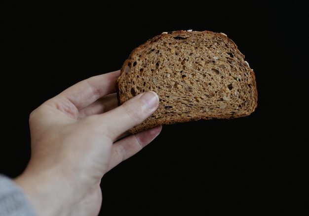 La mano di una donna tiene un pezzo di pane con semi di girasole