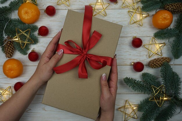 La mano di una donna tiene un regalo in una confezione artigianale con un fiocco di raso rosso