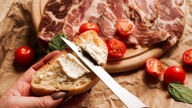 La mano di una donna tiene una bruschetta e si diffonde la ricotta con un coltello