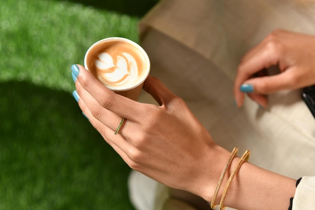 La mano di una donna tiene una tazza di caffè con un disegno di latte.