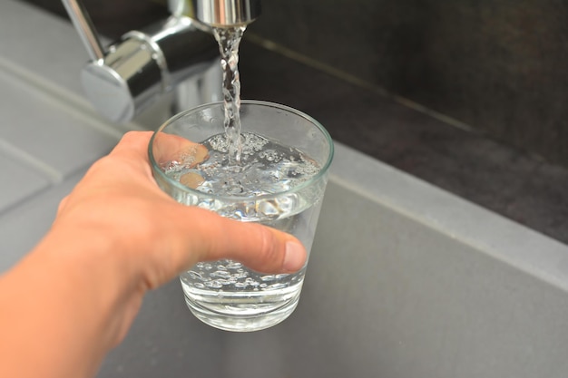 La mano di una donna versa l'acqua in un bicchiere