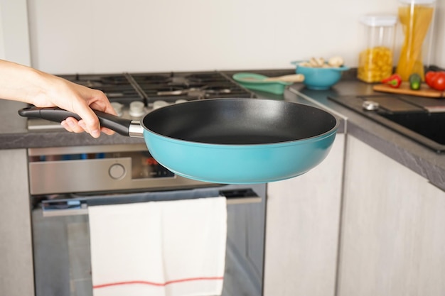 La mano di una giovane donna tiene una nuova padella sullo sfondo della cucina