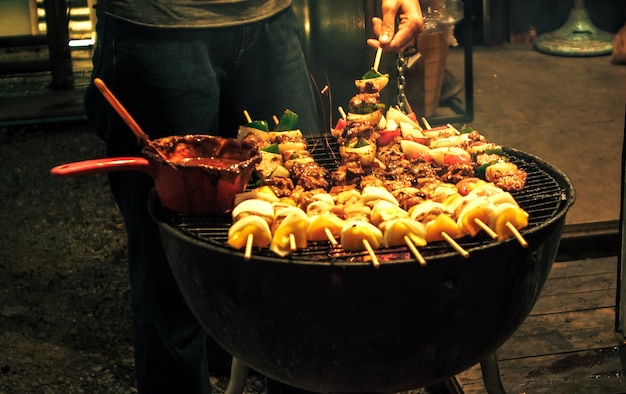 La mano di una persona che spalma la salsa sulla bistecca alla griglia sul barbecue. Barbecue estivo o primaverile all'aperto Primo piano Barbecue gourmet da acquolina in bocca sul tagliere di legno al tavolo.