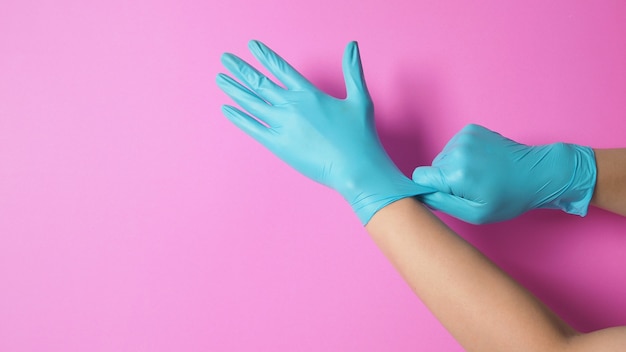 La mano è indossare e tirare guanti in lattice blu o guanti da medico su sfondo rosa.
