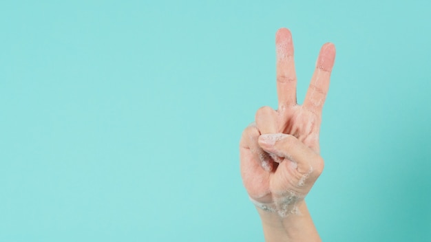 La mano è la vittoria o il segno della mano v e hanno bolle di sapone di schiuma su uno sfondo verde menta o Tiffany Blue