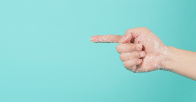 La mano è puntata e ha bolle di sapone di schiuma su uno sfondo verde menta o Tiffany Blue isolato