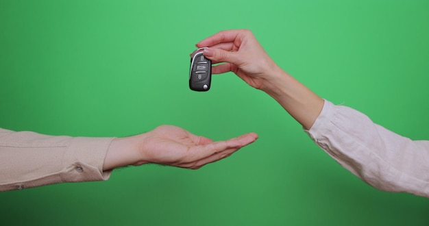 La mano famosa dà le chiavi di una macchina alla mano maschile sullo sfondo verde da vicino