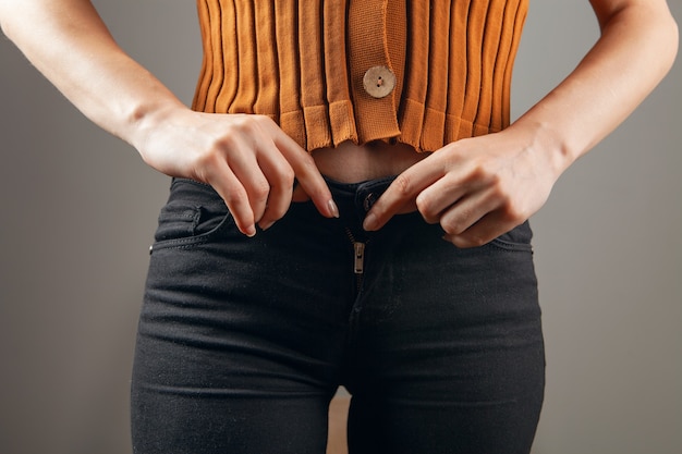 La mano femminile allaccia i jeans su uno sfondo grigio