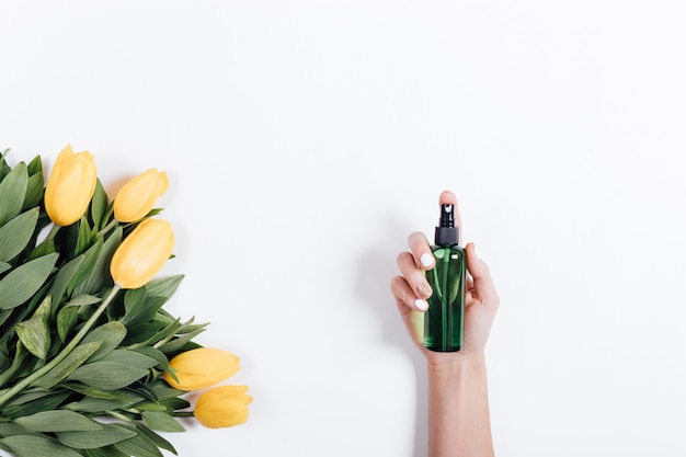 La mano femminile con il manicure tiene una bottiglia di plastica verde dell&#39;acqua vicino ai tulipani gialli, vista dalla cima