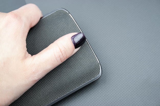 La mano femminile con le unghie scure tiene un telefono cellulare con un dorso in nylon lavorato a maglia che si trova su una cover per laptop grigia testurizzata chiusa