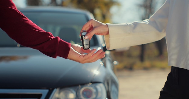 La mano femminile dà le chiavi di una macchina alla mano maschile nella concessionaria auto da vicino. Venditore di auto non riconosciuto e una donna che ha acquistato un veicolo.