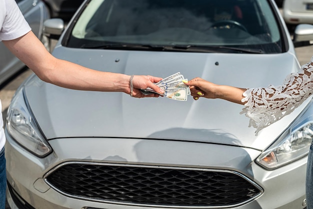 La mano femminile dà un dollaro a un venditore al momento dell'acquisto di una nuova auto moderna, concetto di vendita