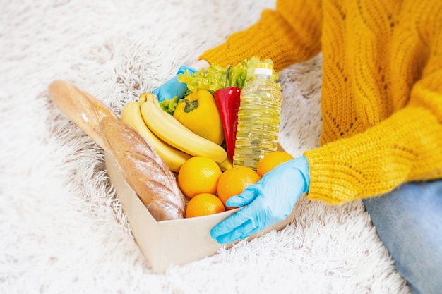 La mano femminile in guanti medici blu tiene una scatola di cartone con alimento vegano