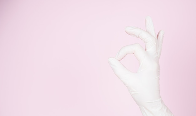 La mano femminile in guanto monouso mostra OK, isolata su sfondo rosa con spazio per le copie.