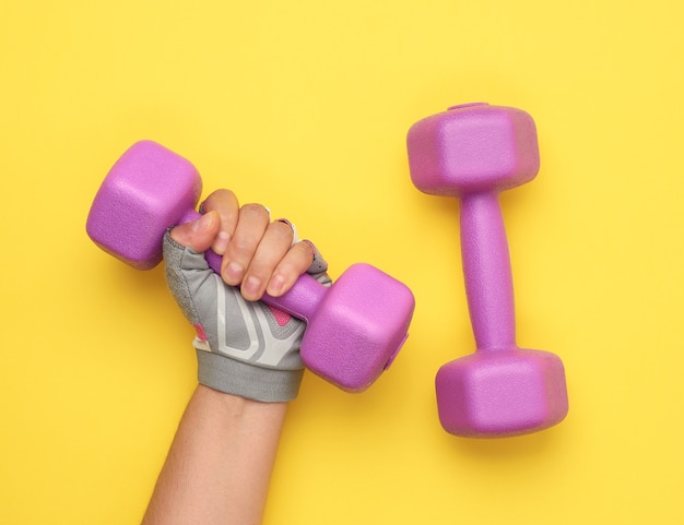 La mano femminile in un guanto sportivo rosa tiene un manubrio viola da un chilogrammo