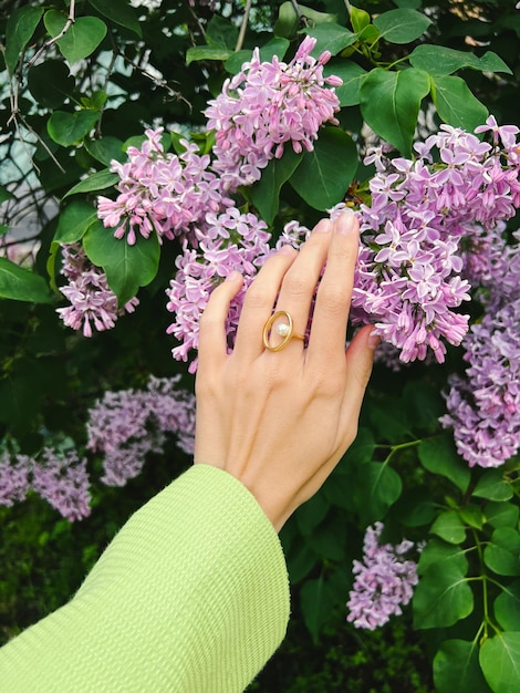 La mano femminile in una giacca verde e un anello di gioielli d'oro tiene un fiore lilla.