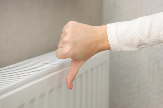 La mano femminile mostra un pollice in giù sullo sfondo di un radiatore senza riscaldamento a freddo