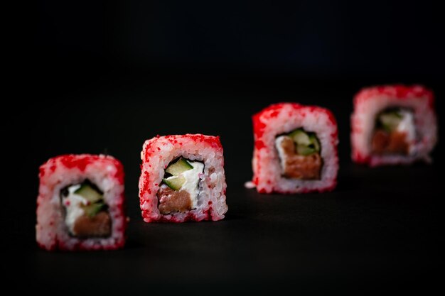 La mano femminile prende i rotoli di sushi della california con le bacchette cinesi Fuoco selettivo sfondo nero