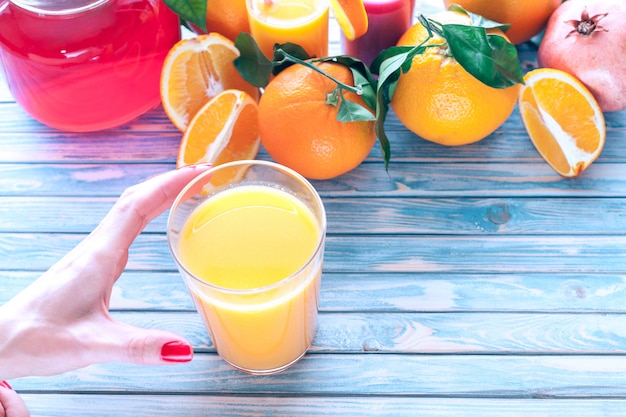 La mano femminile raggiunge per il succo di arancia appena spremuto su legno blu