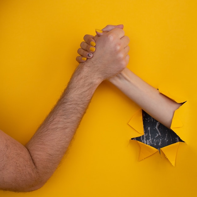 La mano femminile scuote il maschio da un buco in uno sfondo giallo strappato. concetto di aiuto