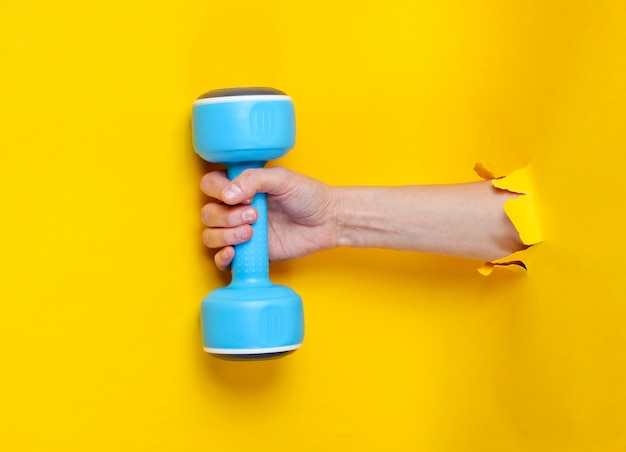 La mano femminile sta tenendo la testa di legno blu attraverso la carta gialla lacerata. Concetto di sport minimalista