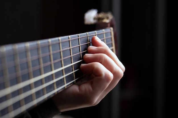 La mano femminile stringe un accordo su una chitarra acustica.