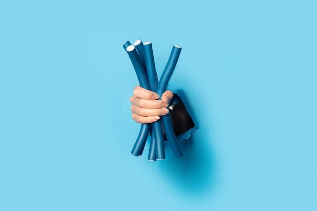 La mano femminile tiene i bigodini blu del papillote su un fondo blu luminoso