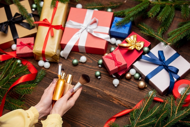 La mano femminile tiene i cosmetici vicino ai regali di Natale