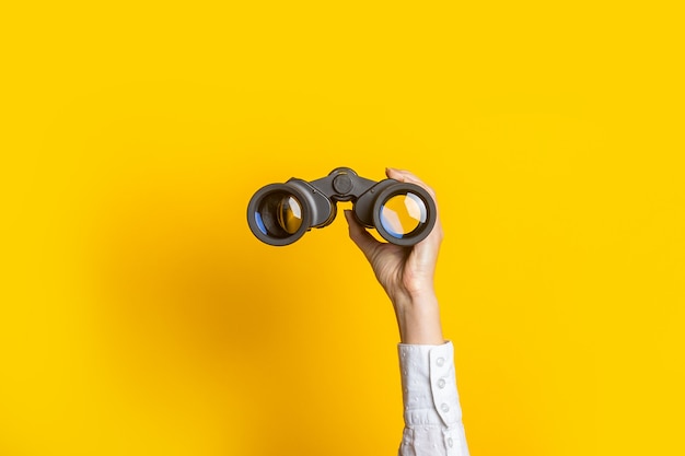 La mano femminile tiene il binocolo nero su uno sfondo giallo brillante