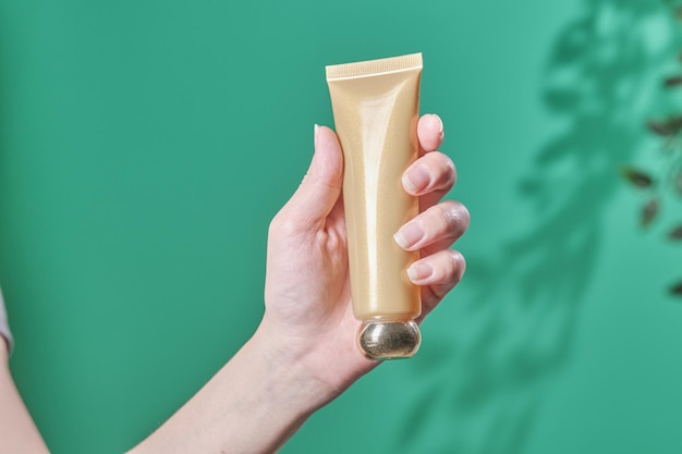 La mano femminile tiene il prodotto cosmetico nella crema idratante antietà della lozione della bottiglia di vetro del tubo