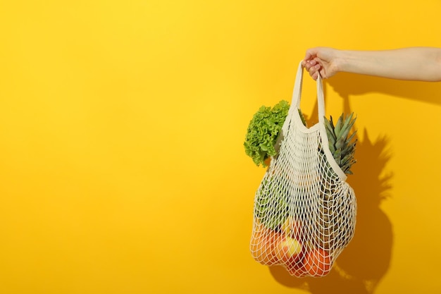 La mano femminile tiene la borsa della stringa con il cibo su sfondo giallo