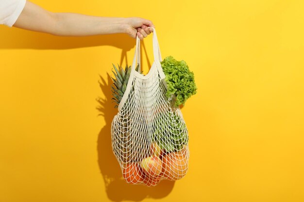 La mano femminile tiene la borsa della stringa con il cibo su sfondo giallo