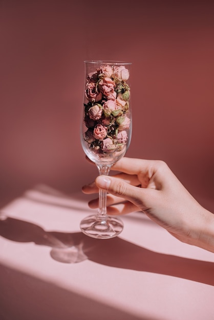 La mano femminile tiene un bicchiere di vino con rose secche su una rosa