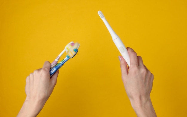 La mano femminile tiene un moderno spazzolino elettrico con caricatore su colore giallo.