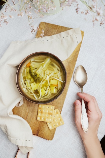 La mano femminile tiene una ciotola di cucchiaio di zuppa vegetariana sul tavolo