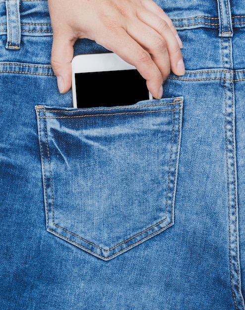 La mano femminile tira fuori dalla tasca posteriore di uno smartphone blu jeans