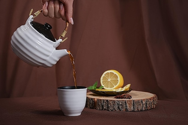 la mano femminile versa il tè in una tazza. accanto al limone e alla menta