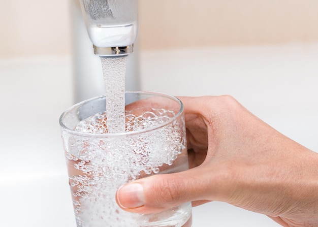 La mano femminile versa l'acqua dal rubinetto in un bicchiere