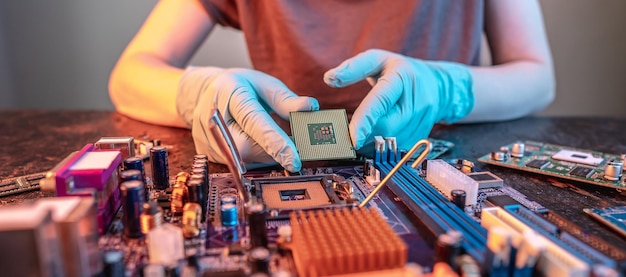 La mano guantata dell'ingegnere tiene il chip della CPU sullo sfondo della microelettronica hardware Hightech della scheda madre