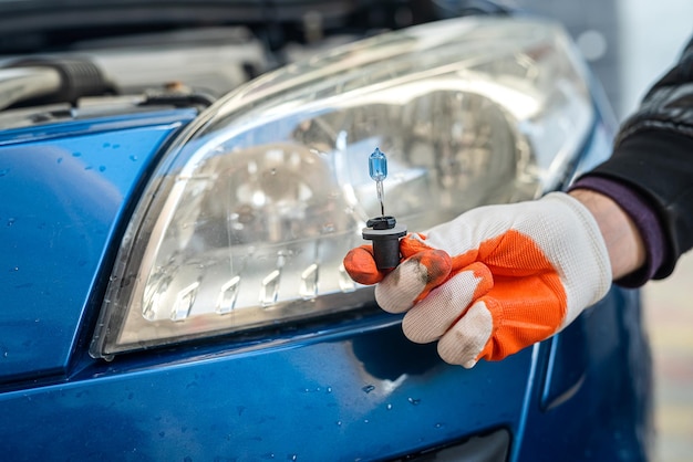 La mano guantata tiene una lampada gelagon vicino ai fari di un'auto blu