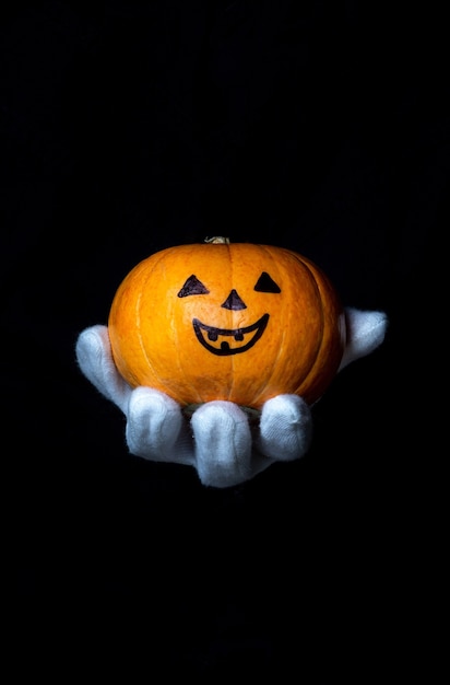 La mano in un guanto bianco tiene una zucca su uno sfondo nero