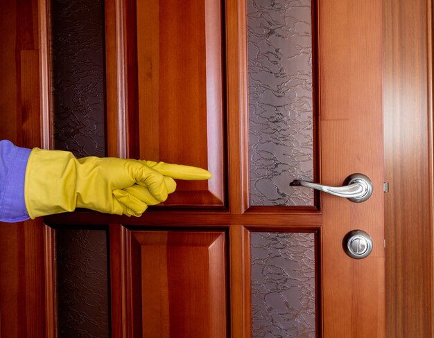 La mano in un guanto di gomma indica la maniglia della porta. disinfezione durante l'epidemia di virus. pulizia dell'appartamento. pulizia della maniglia della porta