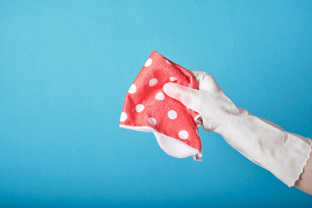 La mano in un guanto di gomma tiene lo straccio rosa su sfondo blu copia spazio