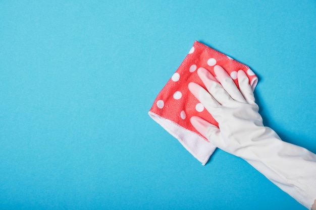 La mano in un guanto di gomma tiene lo straccio rosa su sfondo blu copia spazio