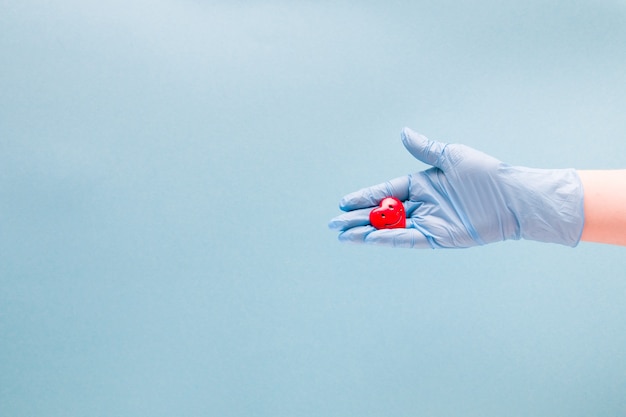 la mano in un guanto tiene un piccolo cuore sorridente rosso