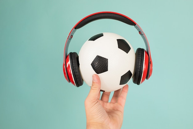 La mano mantiene una palla colorata per il basket con gli auricolari rossi ascolta la musica isolata su sfondo blu