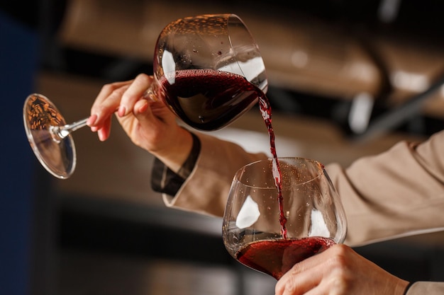 La mano maschile tiene bellissimi calici trasparenti per vino bordeaux in cui il vino rosso viene versato da un altro calici