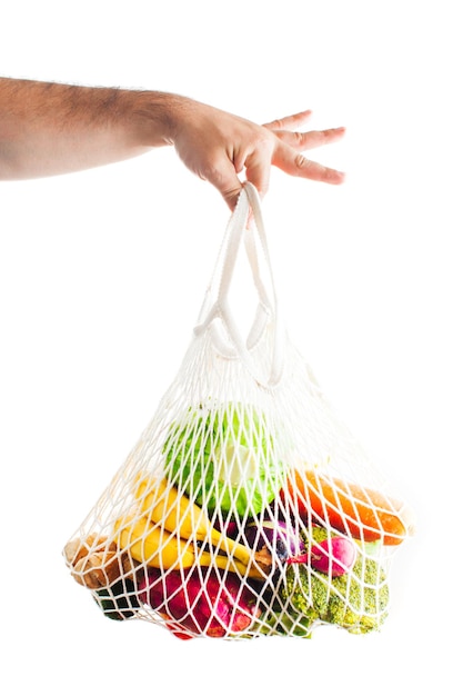 La mano maschile tiene una borsa in rete di cotone con frutta e verdura fresca. Concetto di mercato alimentare biologico